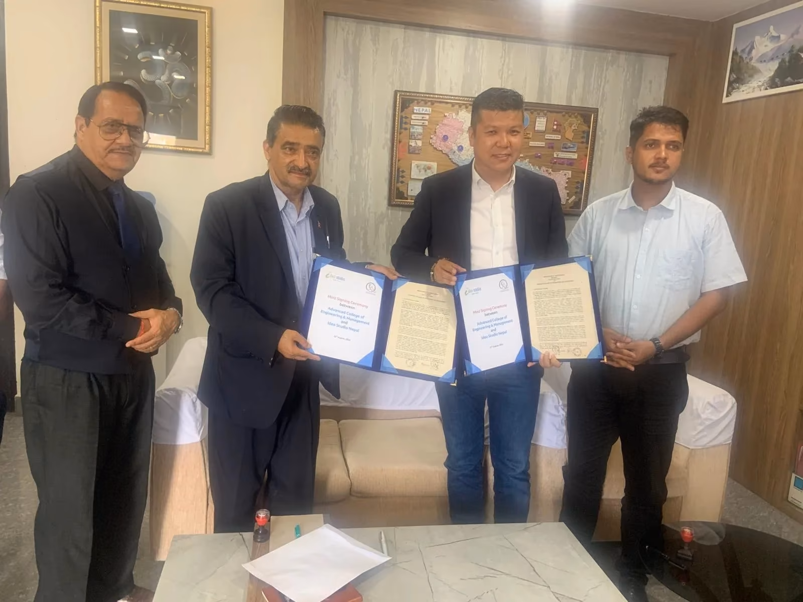 Four men holding two signed agreement folders open for the camera in an office