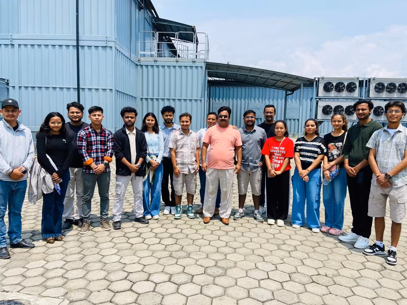 Students outside a steel-clad plant building on a visit, its cooling units ranged along the wall