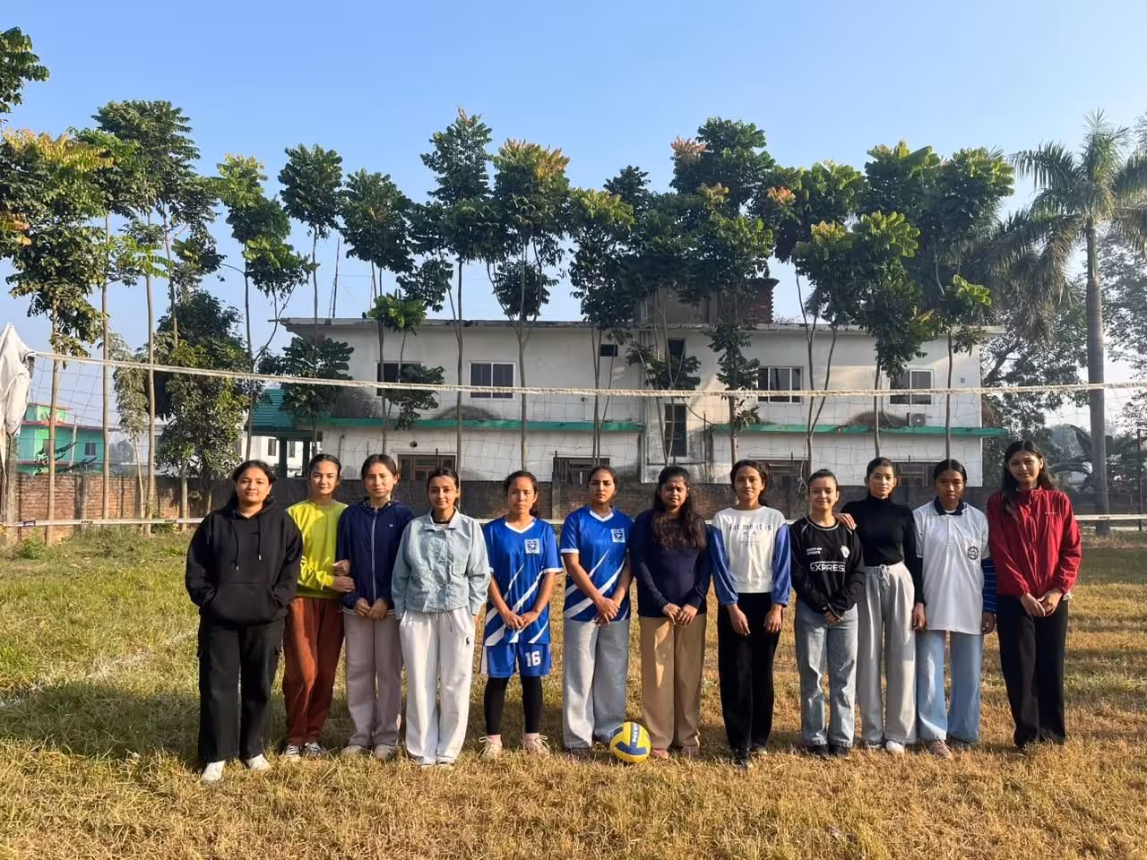 Members of the volleyball side on the grass of the college sports ground, campus buildings behind