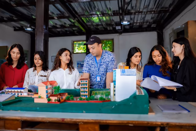 Students and a tutor round a table of architectural scale models, streets and blocks laid out on a base