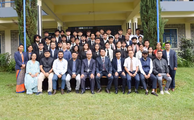 A large cohort of students and staff seated and standing on the lawn