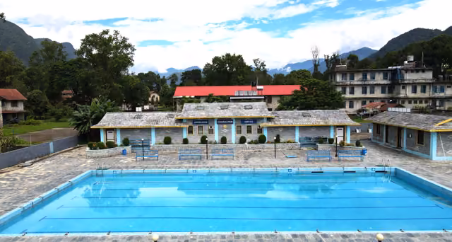 The campus swimming pool in front of a long low block, hills behind it