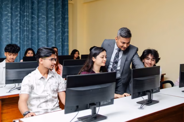 A tutor leaning over students at their monitors in the computer laboratory
