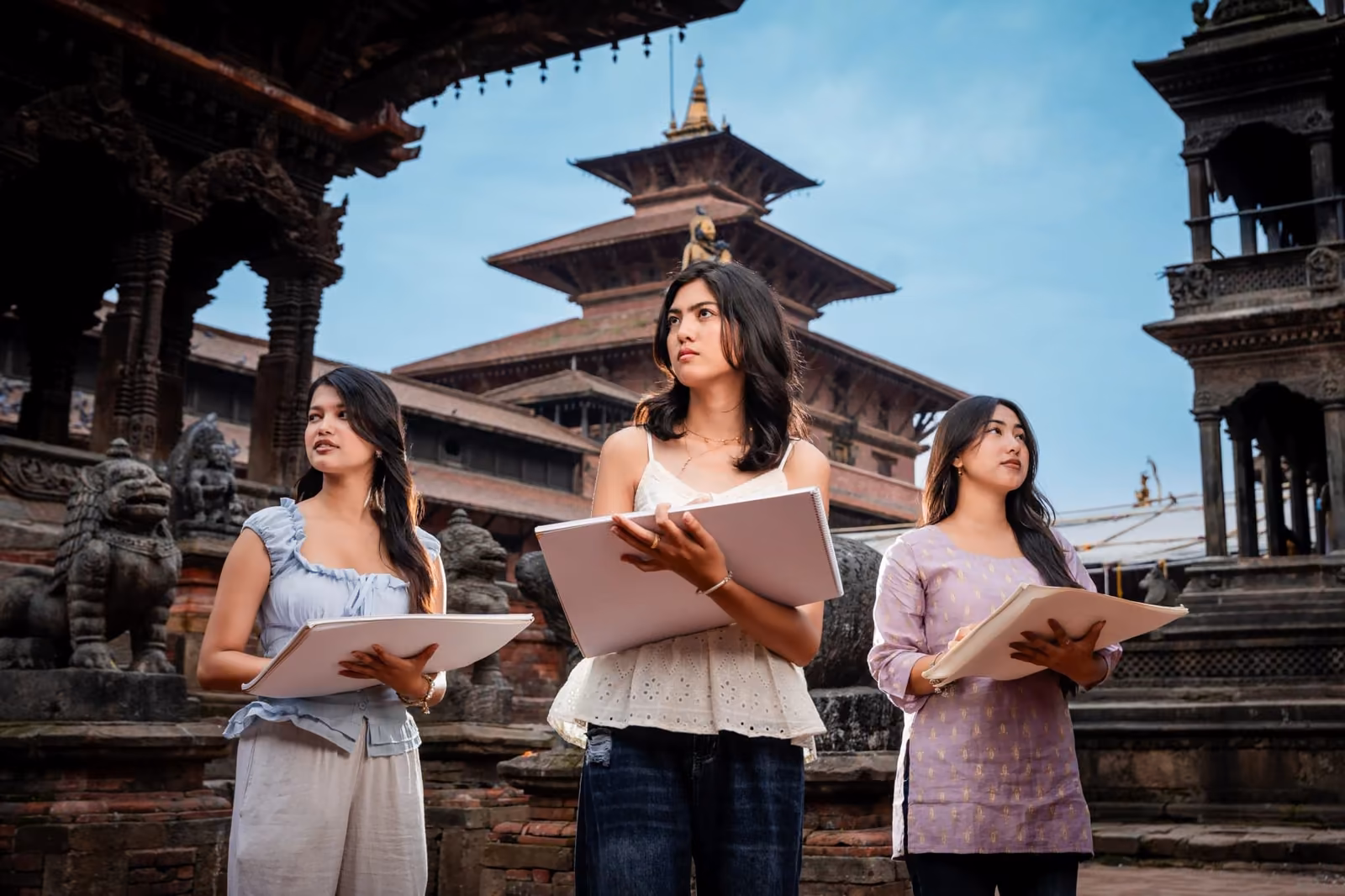 Three students with laptops in front of a tiered temple on a durbar square