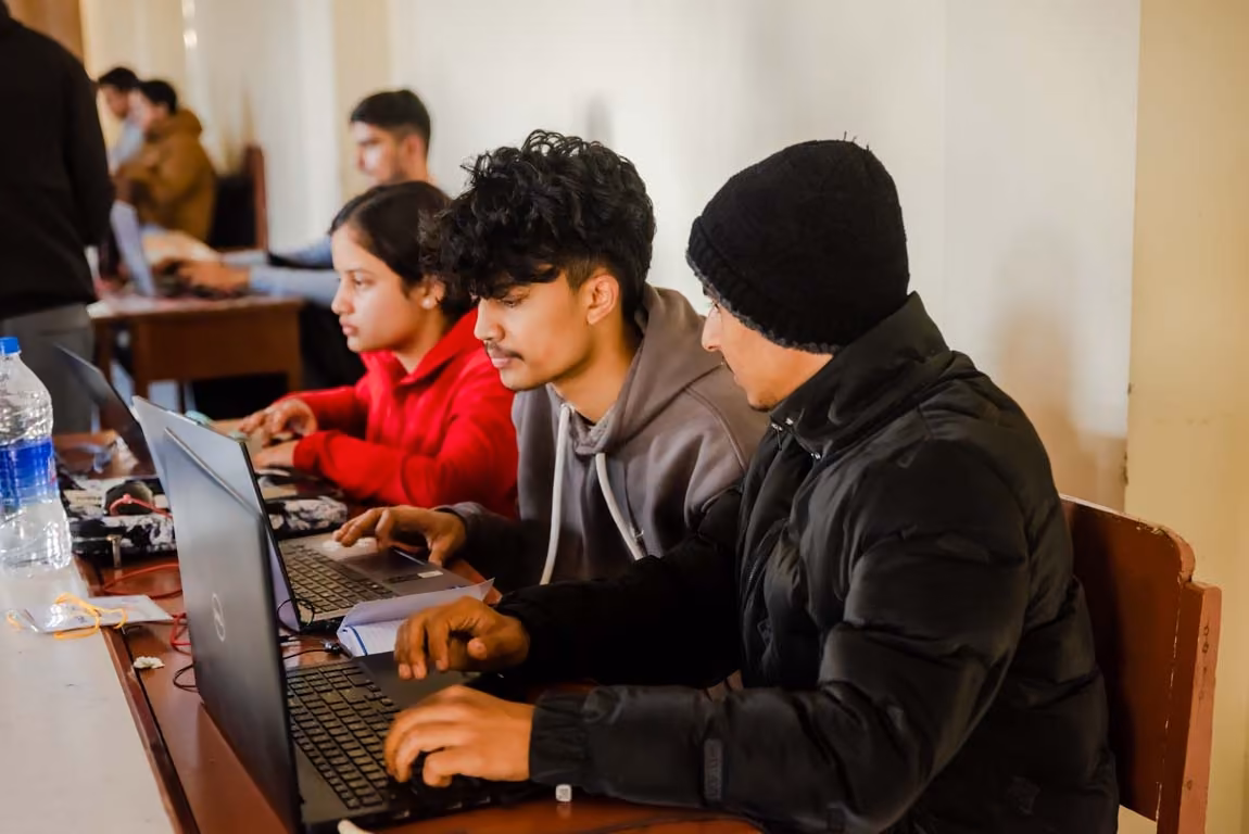 Students working at laptops along the benches of a crowded hall