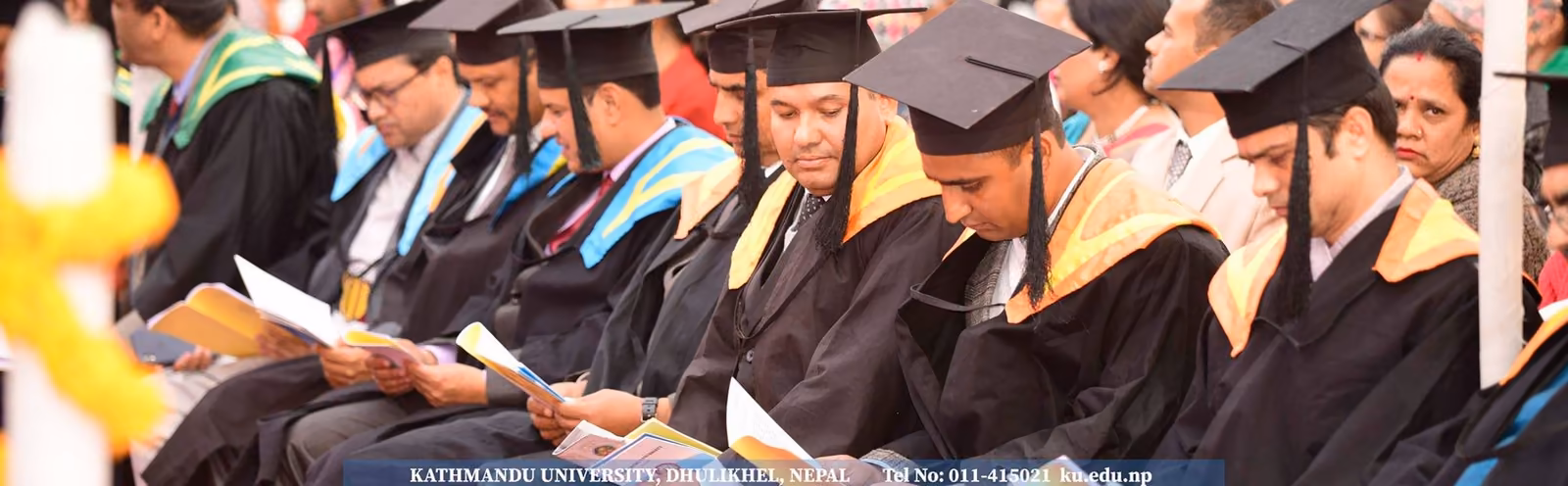 A row of graduands in cap and gown reading their programmes at a convocation