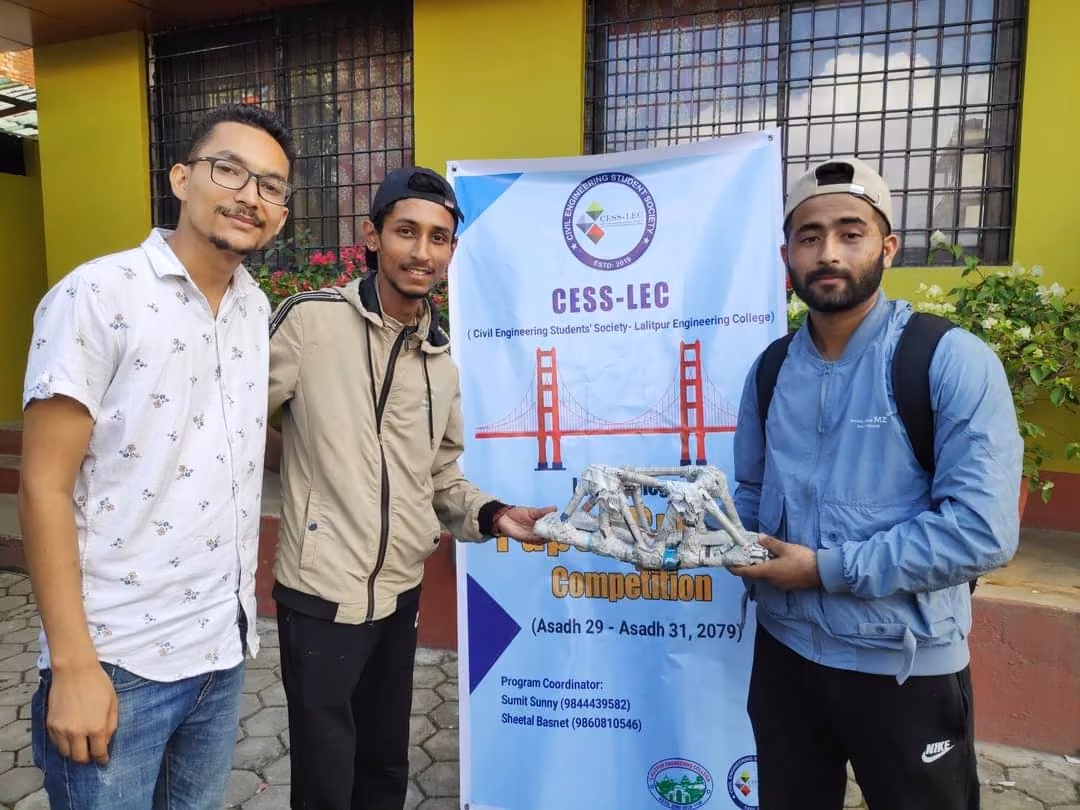 Three students holding a model truss bridge they built for a student society competition