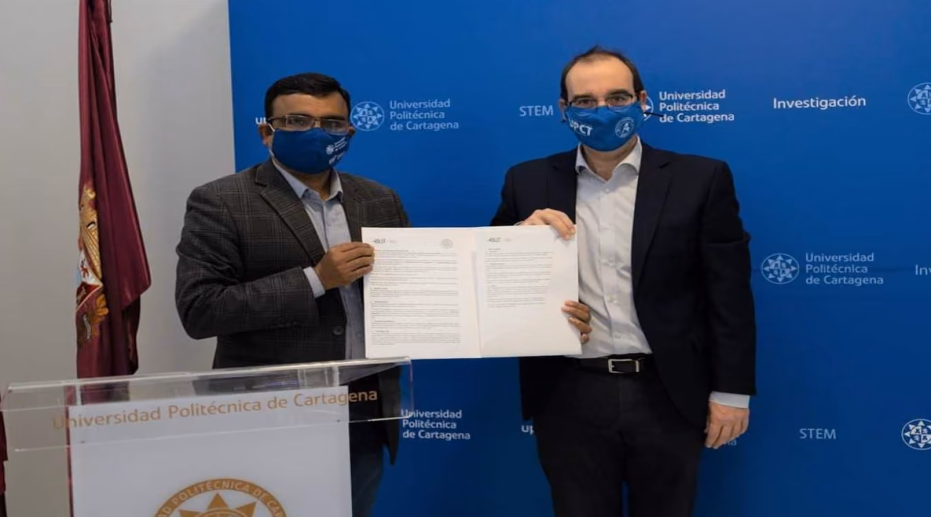 Two men holding a signed agreement at a lectern branded Universidad Politecnica de Cartagena
