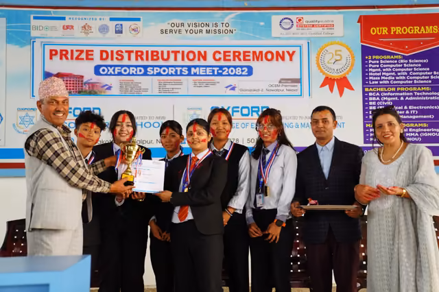 Students holding a trophy and certificates at the sports meet prize ceremony, staff beside them
