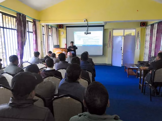 An audience filling a lecture room, a slide projected at the front