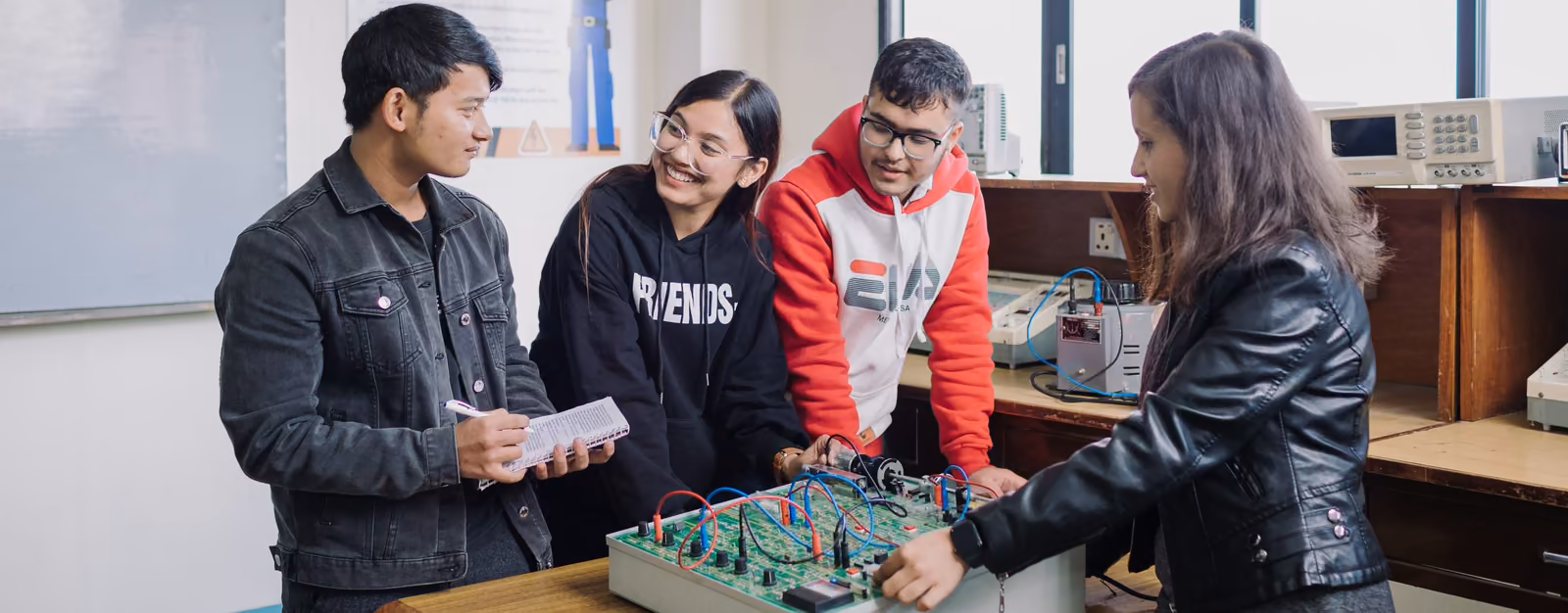 A tutor and four students round a circuit board on a laboratory bench